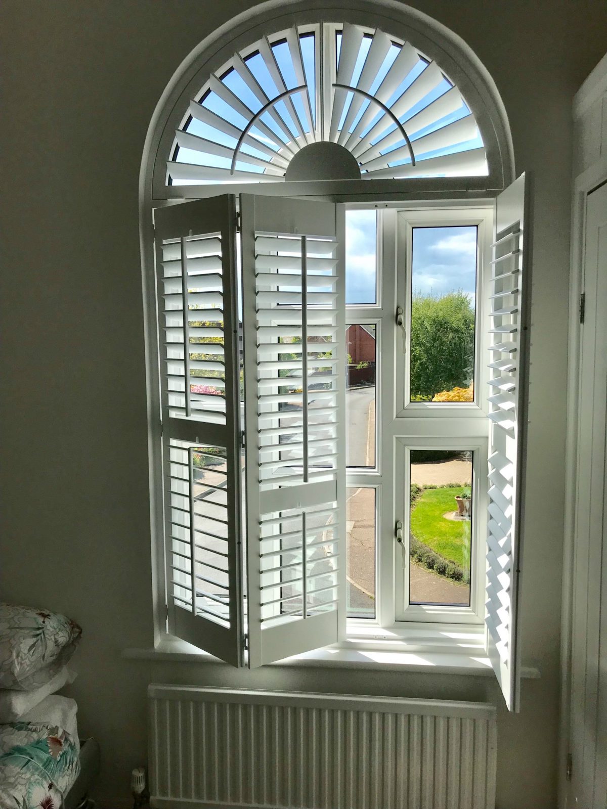 Folding wooden shutters with arched window frame in romford