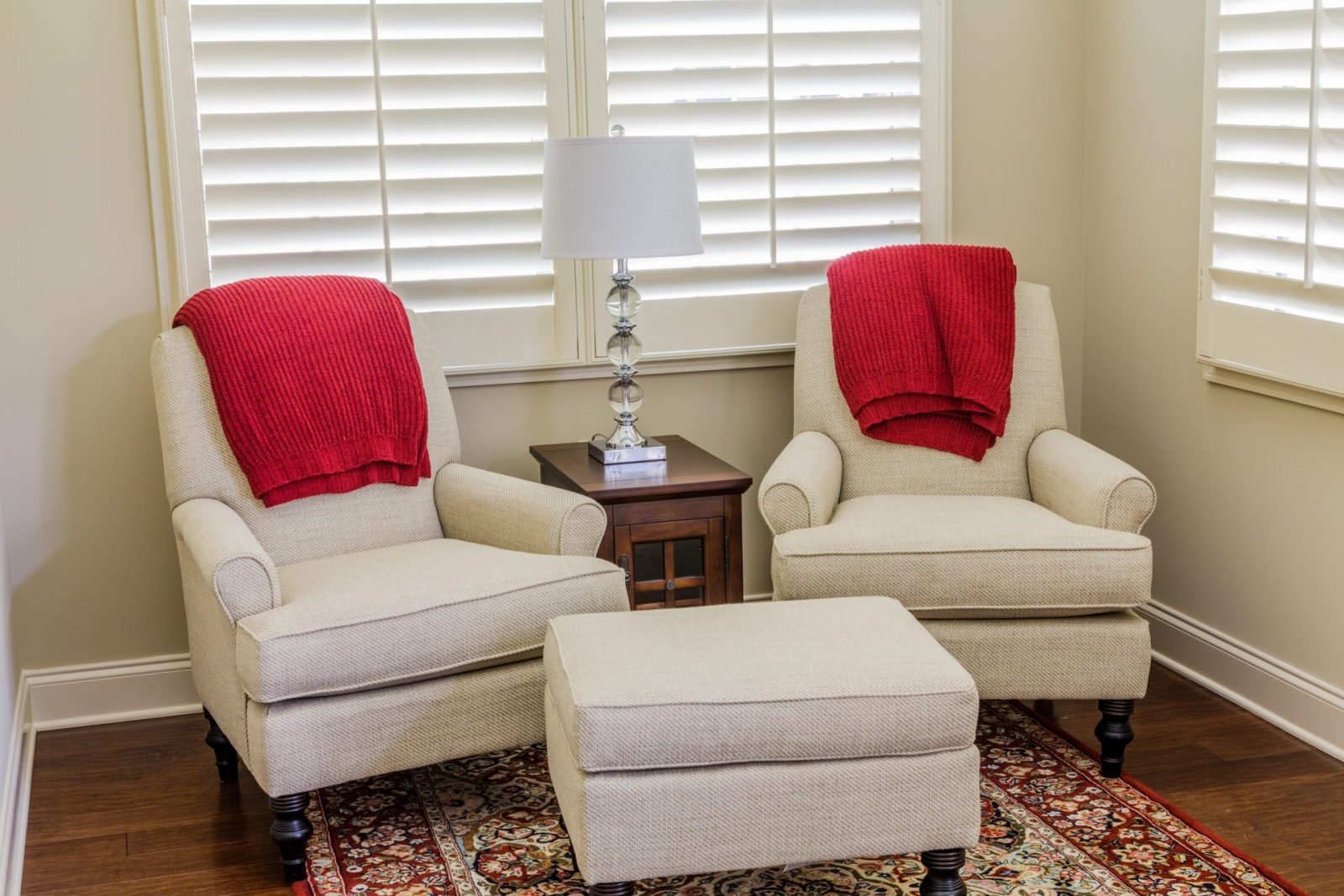 Two white arm chairs with red cusions infront of wooden shutters